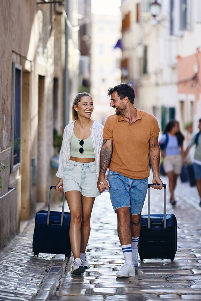 happy couple of tourists dragging their suitcases on the street.